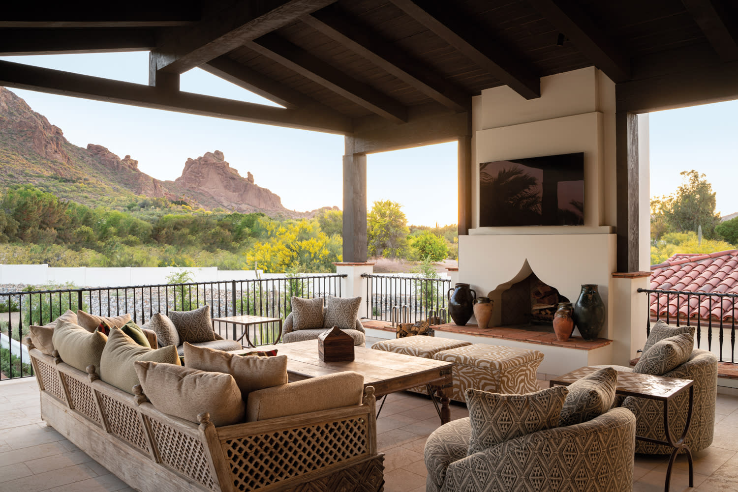 Covered outdoor lounge space with a TV over a fireplace, patterned taupe seating and mountain views