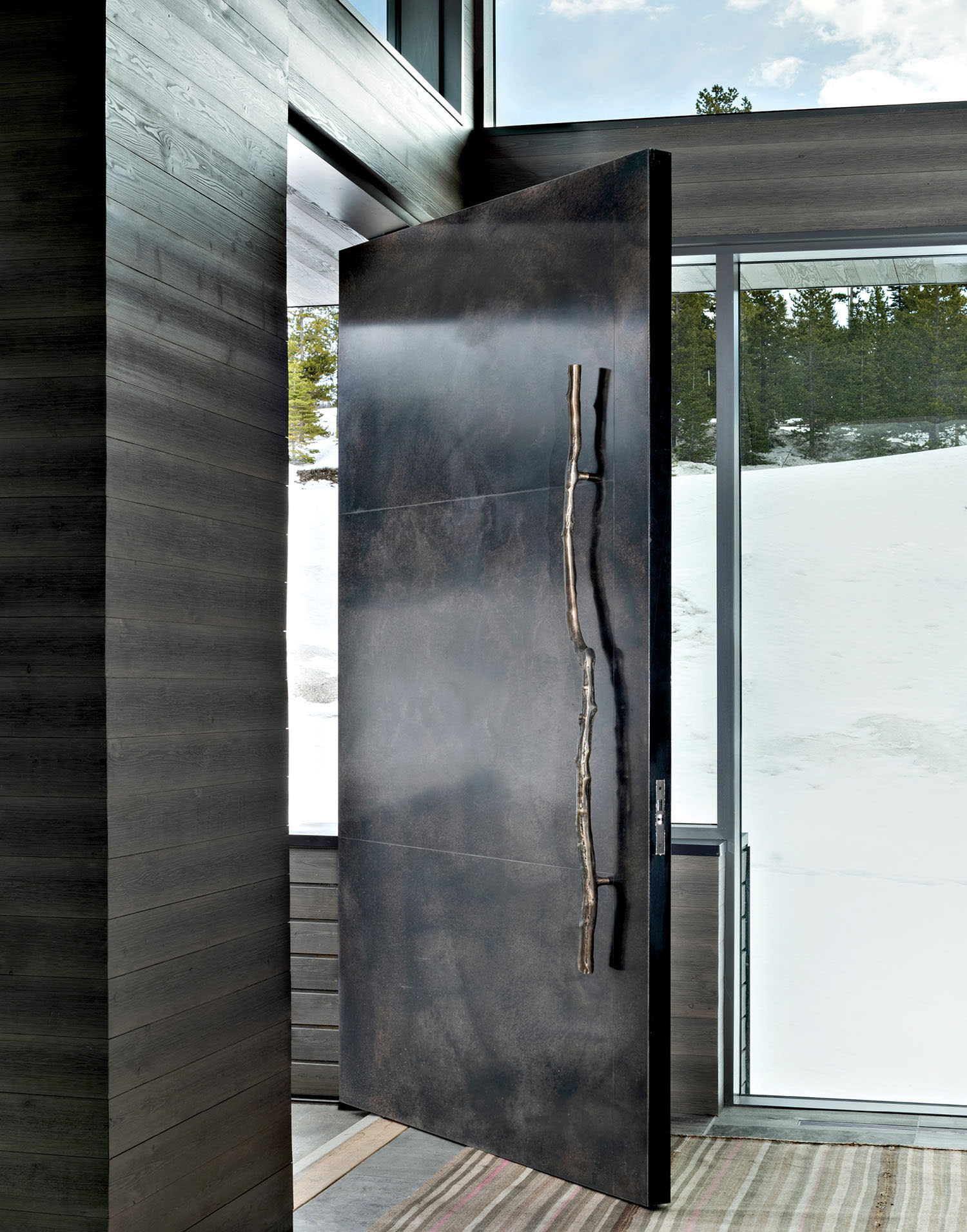 entryway with a custom pivot door made of patinated stainless steel panels and a cast-bronze handle