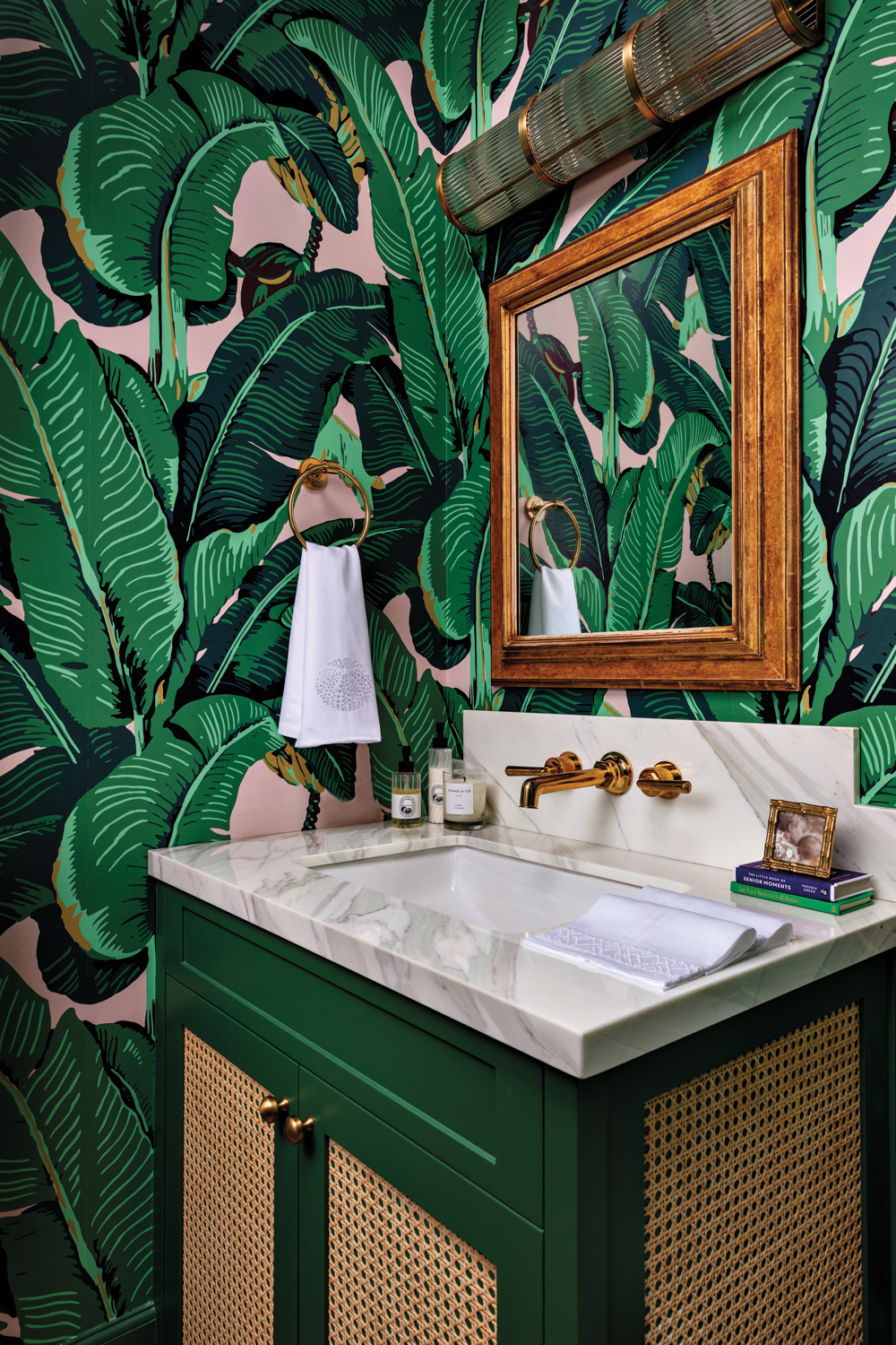 green powder room with banana leaf-print wallpaper and deep green cabinets