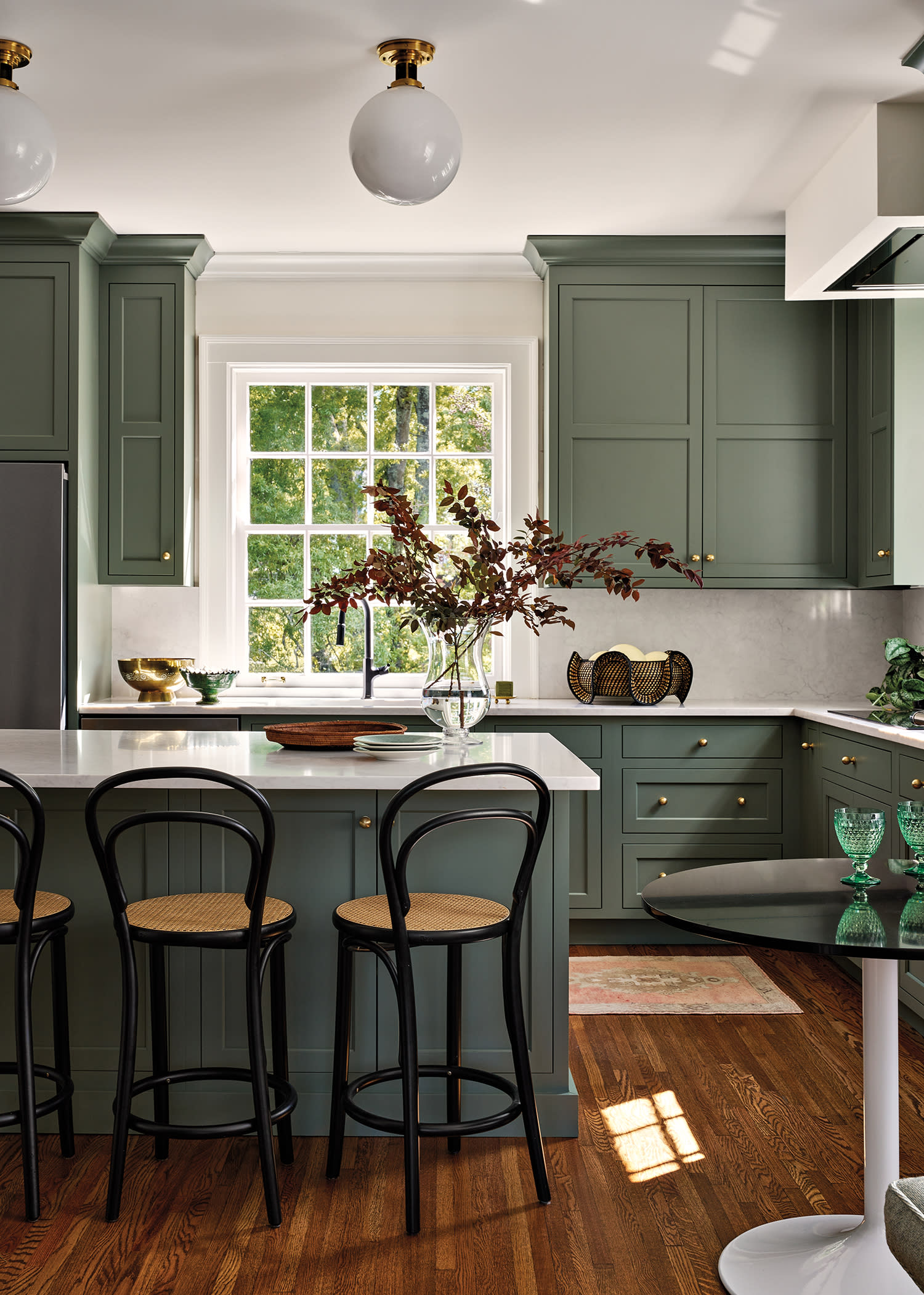 classic kitchen with green cabinetry and black barstools pulled up to a white quartzite island